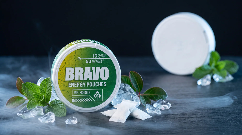 Bravo Wintergreen caffeine pouch tin in sharp focus with mint leaves and frost, one small unbranded pouch tin blurred in the background — Roon focus pouches review hero