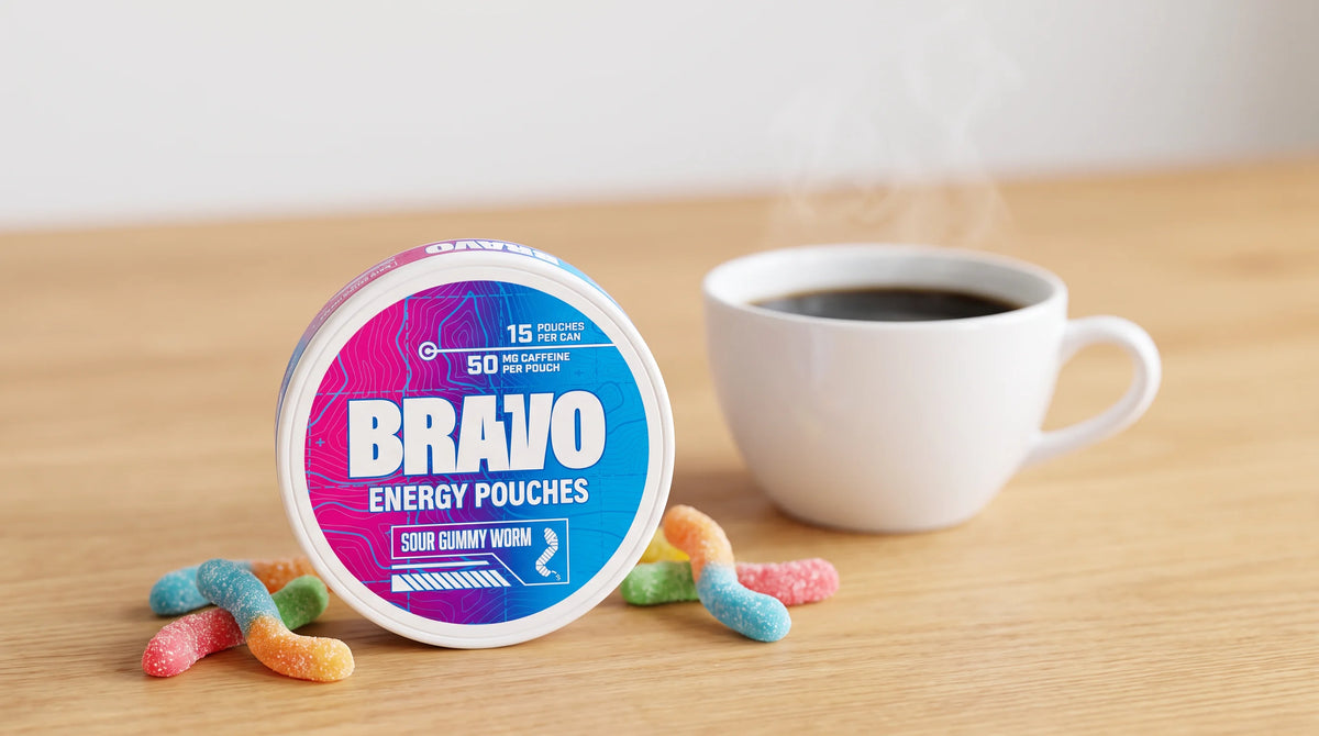 Bravo Sour Gummy caffeine pouch can in sharp focus in the foreground next to a softly blurred cup of coffee, with loose sour gummy candies scattered nearby