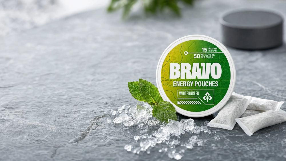 Bravo Wintergreen caffeine pouch can with fresh mint, ice, and loose pouches on a slate surface